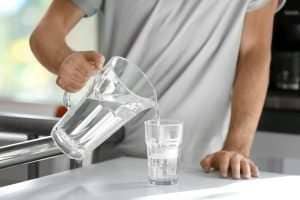 man pouring a glass of filtered water from a pitcher at kitchen counter