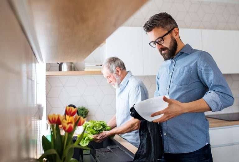 father and adult son washing dishes at kitchen sink